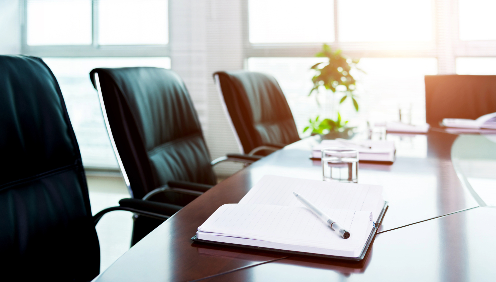 A board room table with seats around it and a notebook on the table